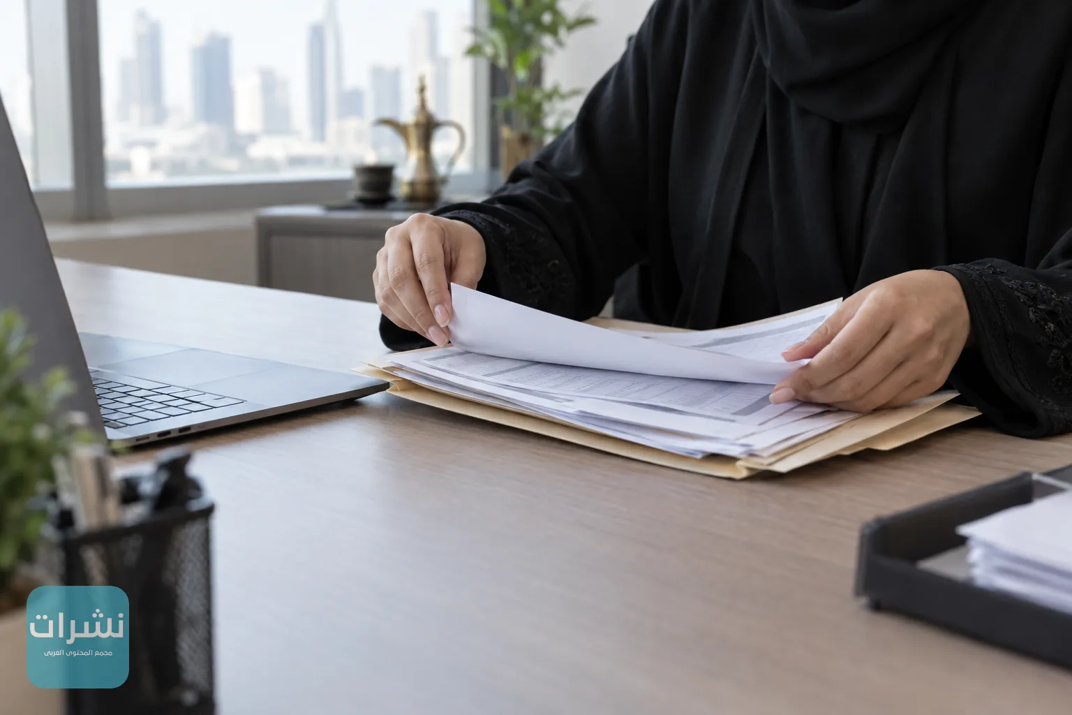 يد ترتب فواتير مبيعات مطبوعة بجانب حاسوب محمول في مكتب صغير